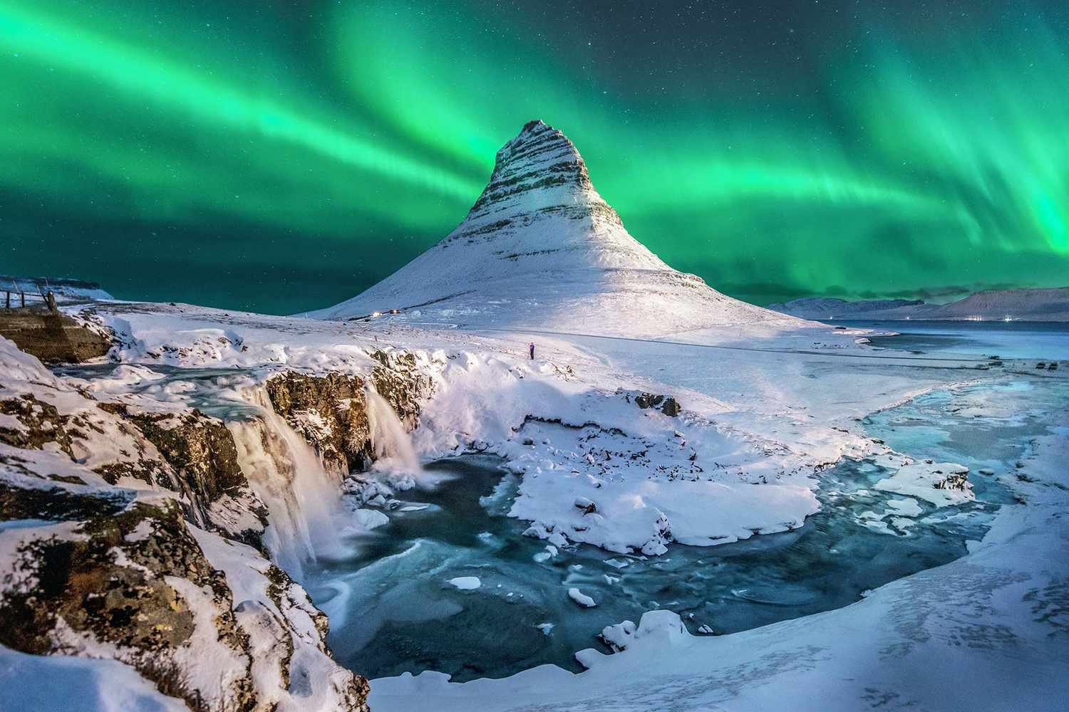 the northern lights in iceland with a hill covered in snow and a frozen stream